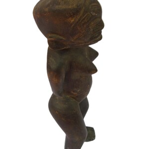 以下が含まれることがあります： 暗い茶色の木彫りの人物像。丸い頭と様式化された体を持つ。木目は見え、アンティークまたはヴィンテージの起源を示唆している。顔の特徴はシンプルに彫刻されている。