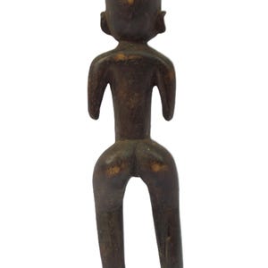 以下が含まれることがあります： 暗い茶色の木製の置物で、様式化された人間の形を描いています。 このフィギュアは丸い頭、小さな耳、腕を広げています。 脚は分離しており、足が底にあります。 彫刻は風化した外観をしています。