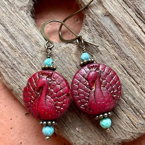 May include: A pair of red peacock earrings with turquoise accents. The earrings are made of clay and have a textured finish.
