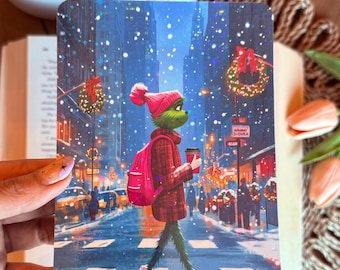 May include: A Christmas-themed illustration depicts a green character in a red coat, hat, and boots, carrying a pink backpack and a coffee cup, walking across a snowy city street. The background shows buildings, traffic, and Christmas decorations.