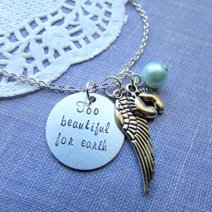 Puede incluir: Collar de plata con un dije que dice "Too beautiful for earth" y un dije de ala de &aacute;ngel de plata. El collar tambi&eacute;n tiene una cuenta azul claro.