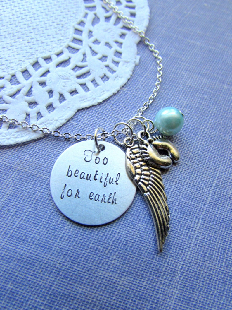 Puede incluir: Collar de plata con un dije que dice "Too beautiful for earth" y un dije de ala de &aacute;ngel de plata. El collar tambi&eacute;n tiene una cuenta azul claro.