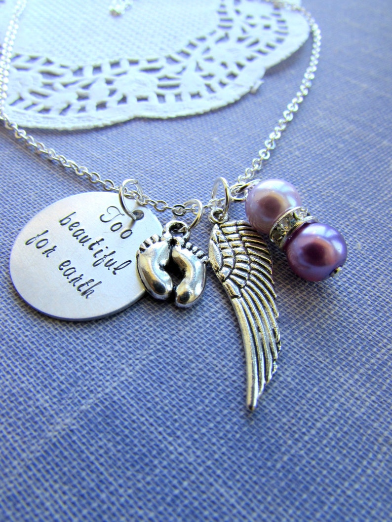 May include: Silver necklace with a charm that reads "Too beautiful for earth" and features a pair of baby footprints, an angel wing, and two purple beads.