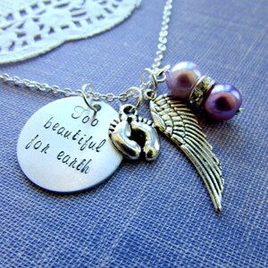 May include: Silver necklace with a charm that reads "Too beautiful for earth", a pair of baby footprints, and a silver angel wing charm. The necklace also features two purple beads.