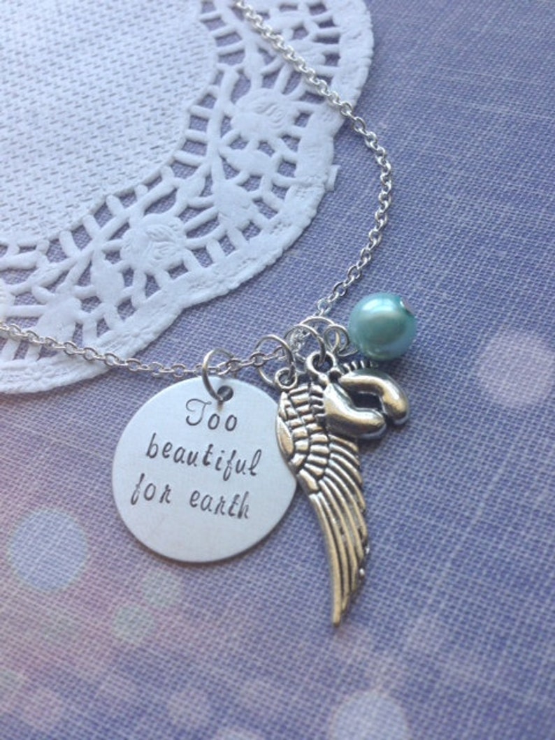 Puede incluir: Collar de plata con un dije que dice "Demasiado hermoso para la tierra" y presenta un ala de &aacute;ngel peque&ntilde;a y una cuenta azul claro.