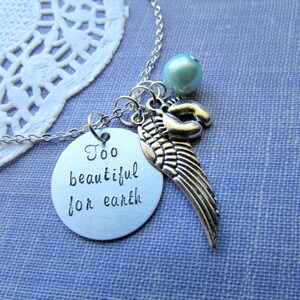 Puede incluir: Collar de plata con un dije redondo que dice "Too beautiful for earth" y un dije de ala de &aacute;ngel de plata. El collar tambi&eacute;n tiene una perla azul claro.