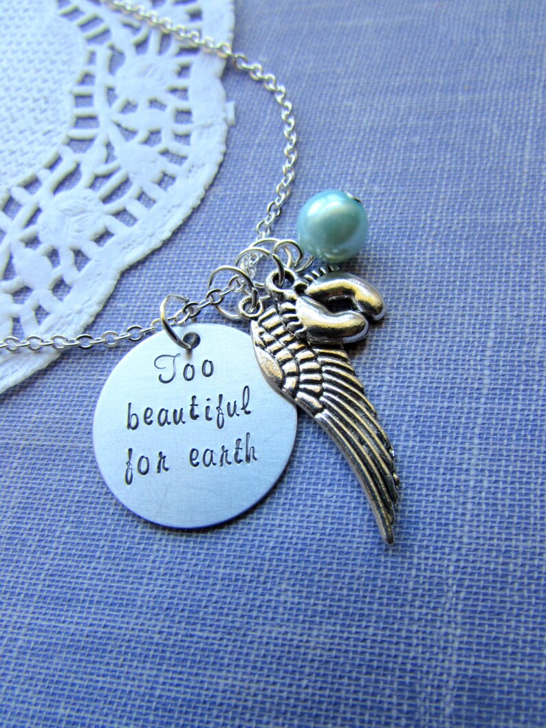 Puede incluir: Collar de plata con un dije redondo que dice "Too beautiful for earth" y un dije de ala de &aacute;ngel de plata. El collar tambi&eacute;n tiene una perla azul claro.