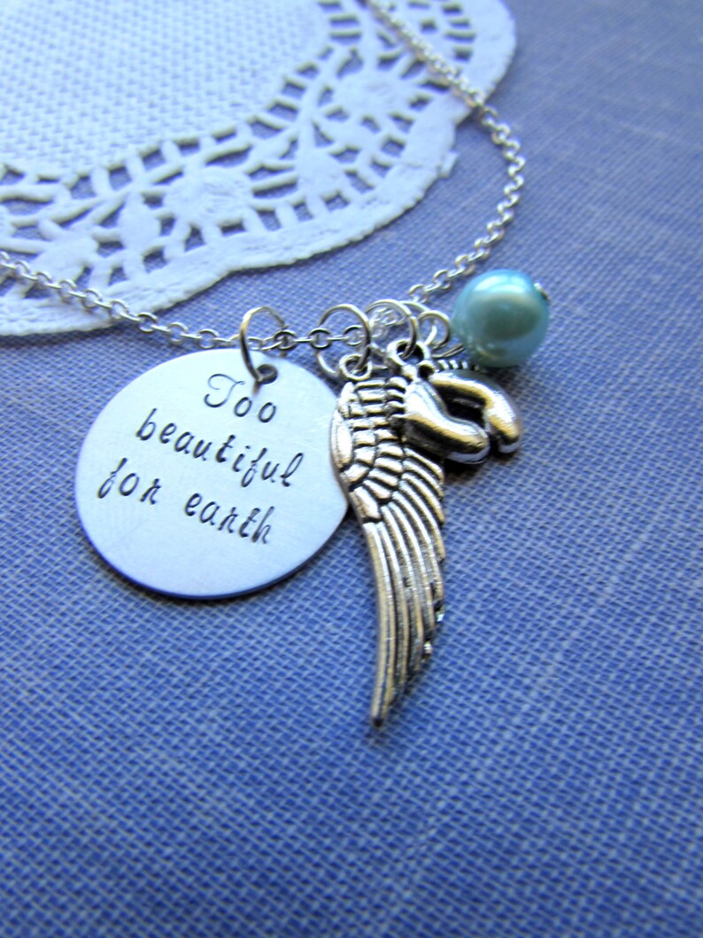 Puede incluir: Collar de plata con un dije que dice "Demasiado hermoso para la tierra" y un dije de ala de &aacute;ngel de plata. El collar tambi&eacute;n tiene una cuenta azul claro.