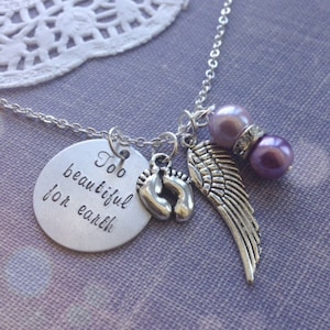 May include: Silver necklace with a round charm that says "Too beautiful for earth" and features a pair of baby footprints, an angel wing, and two purple beads.