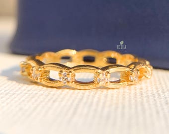 May include: A gold ring with a delicate chain design and small clear stones. The ring is on a white surface.