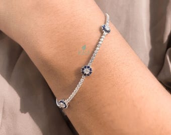 May include: A delicate silver bracelet featuring a line of small, sparkling clear stones. The bracelet is accented with three dark blue flower-shaped charms. The bracelet is worn on a person's wrist.