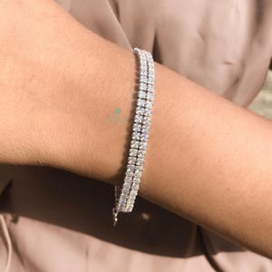 Puede incluir: Un brazalete de tenis plateado con una doble fila de piedras de circonita cúbica transparentes.