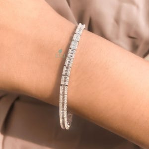May include: A silver tennis bracelet with a row of clear, rectangular-shaped stones.