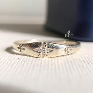 May include: A silver band ring with five small diamonds set in a star shape. The ring is on a white surface.
