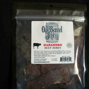 May include: A bag of Oak Barrel Jerky Habanero Beef Jerky. The bag is clear plastic and shows the jerky inside. The label is white with black text and a red barrel logo. The label says "Oak Barrel Jerky" and "Habanero Beef Jerky". The ingredients are listed on the label. The bag is 3 ounces.