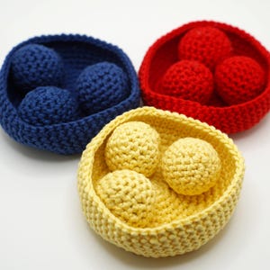 Puede incluir: Tres cestas de crochet, cada una con bolas de crochet. Las cestas son azules, rojas y amarillas. Las bolas son azules, rojas y amarillas.