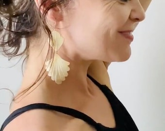 May include: A woman with dark brown hair wearing a black tank top and large gold earrings with a fan-like design.