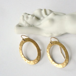 May include: A pair of gold oval-shaped earrings with a hammered texture. The earrings have a simple design and are perfect for everyday wear.