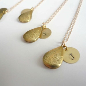 May include: Four gold necklaces featuring teardrop-shaped lockets and round charms. The lockets have a floral design and the charms are engraved with the letters "S" and "J".