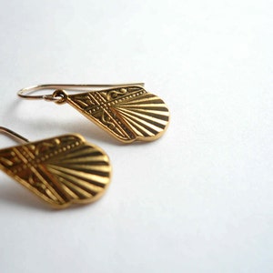 May include: A pair of gold-tone earrings with a fan-shaped design. The earrings are made of metal and have a delicate, intricate pattern.