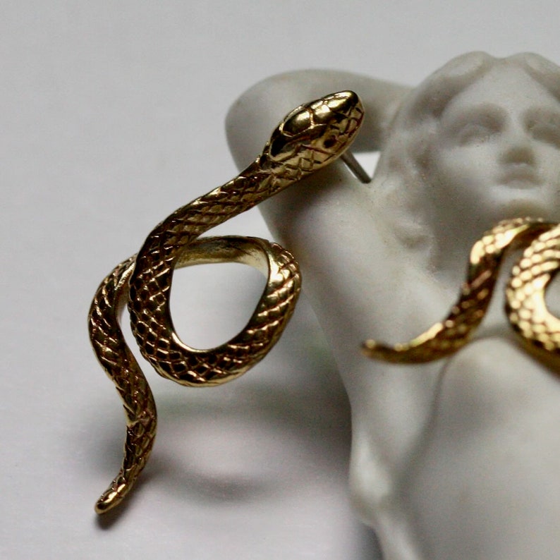 May include: A pair of gold snake earrings. The snakes are curled up and have a textured surface.