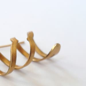 Può includere: Un orecchino aperto dorato, a più strati. L'orecchino è composto da tre pezzi di metallo curvi e intrecciati.