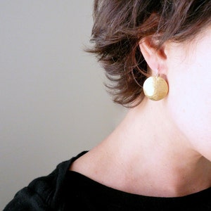 May include: A pair of gold hammered disc earrings. The earrings are round and have a textured surface.