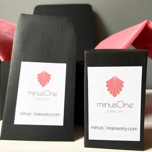 May include: Two black boxes with white labels. The labels feature a pink seashell logo and the text "minusOne JEWELRY" and "minusOnejewelry.com".