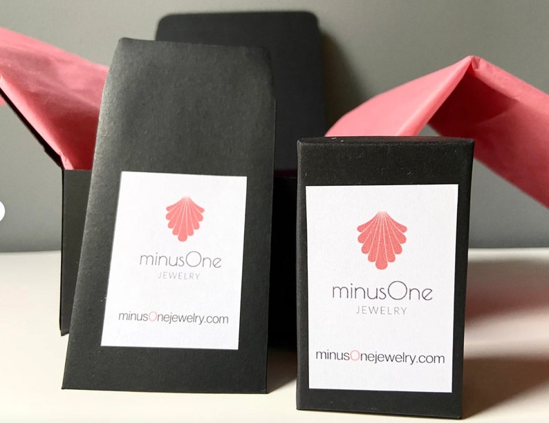 May include: Two black boxes with white labels. The labels feature a pink seashell logo and the text "minusOne JEWELRY" and "minusOnejewelry.com".