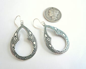 May include: A pair of silver dangle earrings with an intricate, openwork design. The earrings are shaped like teardrops with a geometric pattern.