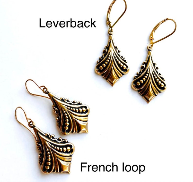 May include: Two pairs of gold-colored earrings. One pair features leverback closures, and the other has French loop closures. Both styles have a decorative, ornate design with a diamond-like shape and a series of small, raised dots.