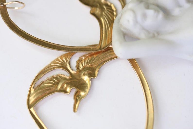 May include: Close-up of a gold-colored, Art Nouveau-style decorative element. The design features stylized bird and leaf motifs, with a white porcelain figure partially visible. The piece has a delicate, ornate appearance.