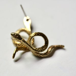 May include: Gold-toned snake earring with a textured surface. The snake is coiled and has a small head with a pointed nose.