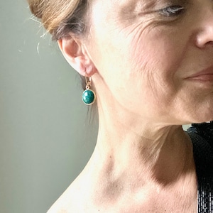 Könnte beinhalten: Goldene Ohrhänger mit einem runden, dunkelgrünen Edelstein.