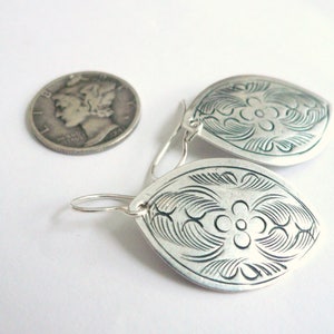 May include: A pair of silver earrings with a floral design. The earrings are shaped like an oval and have a hook closure.