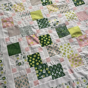 May include: A handmade quilt with a patchwork design featuring squares of various patterns. The quilt incorporates white, pink, green, and tan fabrics. Some squares display pickleball paddles and balls, while others have stripes or polka dots.
