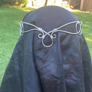 May include: A silver wire headband with a delicate, intricate design. The headband is made of wire that is twisted and shaped into a series of loops and curves.