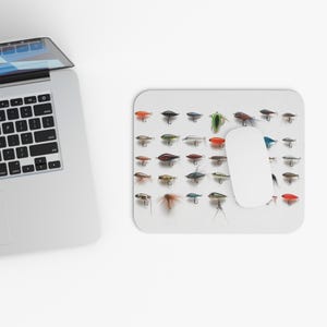 May include: A white mouse pad with a variety of colorful fishing lures arranged in rows. The lures are a mix of different sizes and styles, including some with feathers and some with metal.