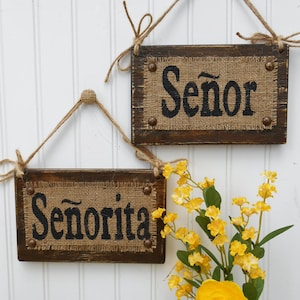 May include: Two rustic wooden signs with burlap fabric and black lettering. The top sign reads "Se&ntilde;or" and the bottom sign reads "Se&ntilde;orita".