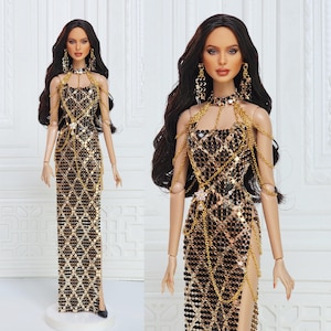 May include: A fashion doll with long dark wavy hair wearing a floor-length black and gold sequined dress featuring a diamond pattern. The doll is adorned with gold chain shoulder straps, a matching gold chain choker, and dangling gold earrings.