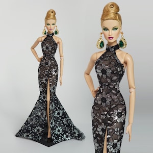 May include: A fashion doll wearing a black and silver sequined gown with a high neckline and a thigh-high slit. The doll has blonde hair styled in a high bun and is wearing large green and gold earrings.