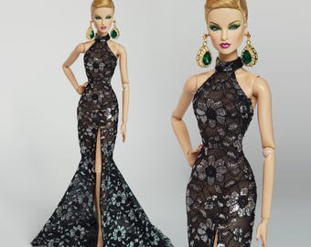 May include: A fashion doll wearing a black and silver sequined gown with a high neckline and a thigh-high slit. The doll has blonde hair styled in a high bun and is wearing large green and gold earrings.