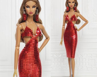 May include: Two dolls wearing red sequin dresses and matching earrings. The dresses have a halter top and a knee-length skirt. The dolls have long brown hair and are posed in front of a white background. The dresses are covered in small, shiny sequins.