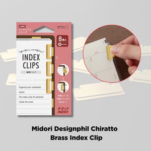 Puede incluir: Un paquete de clips de índice de latón Midori Designphil Chiratto. El paquete es rosa y negro, con el texto "INDEX CLIPS" y "8 M size". La imagen también muestra a una persona usando el clip de latón en una página de calendario.