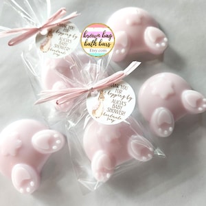 K&ouml;nnte beinhalten: Rosa, hasenf&ouml;rmige Seifen, verpackt in transparenten Zellophanbeuteln und mit rosa Bastb&auml;ndern gebunden. Jede Seife hat wei&szlig;e Pfoten-Details. Die Seifen sind mit "ALICIA'S BABY SHOWER! handmade soap" beschriftet. Der Etsy-Shop-Name "brown bag bath bars" ist ebenfalls sichtbar.