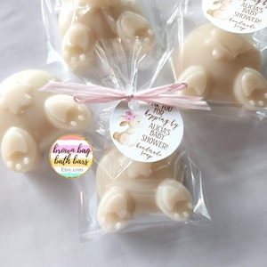 May include: Ivory-colored bunny-shaped soaps, individually wrapped in clear cellophane. Each soap is tied with a pink ribbon and a circular tag that reads "Alicia's Baby Shower! handmade soap". The soaps are from brown bag bath bars.