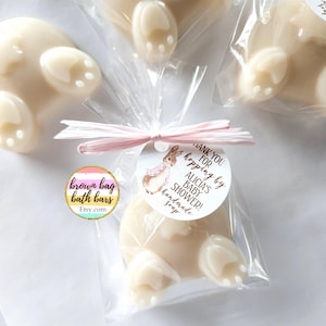 K&ouml;nnte beinhalten: Handgemachte Seifen in Hasenform, einzeln in durchsichtigem Zellophan verpackt und mit rosa Band gebunden. Jede Seife hat ein Etikett mit der Aufschrift "Thank you for hopping by Alicia's Baby Shower!" und eine Aquarell-Hasen-Illustration.