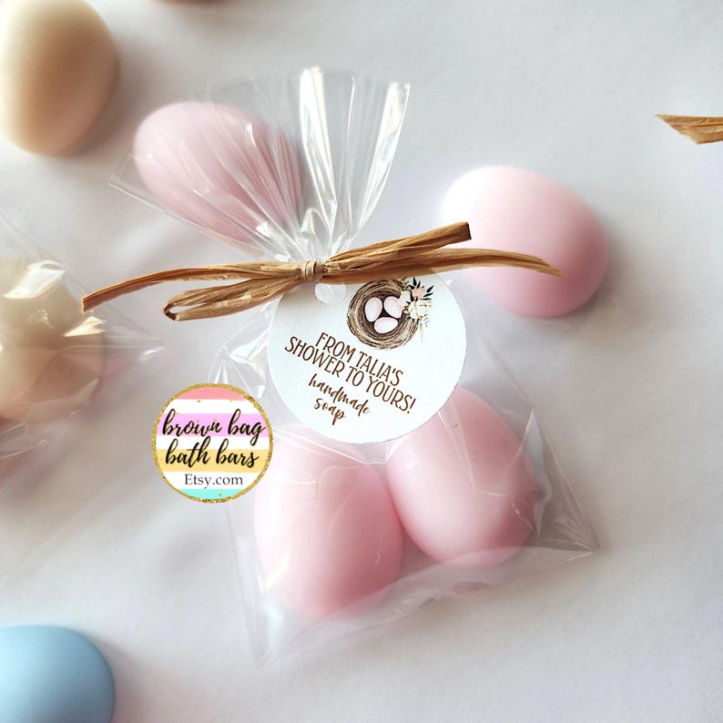 May include: Pink egg-shaped soaps in clear cellophane bags, tied with raffia and a round tag. The tag reads "From Talia's Shower to Yours! handmade soap" with a nest illustration. The soaps are from brown bag bath bars.