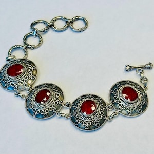 May include: A silver bracelet with four red gemstone cabochons set in ornate silver bezels. The bracelet has a toggle clasp.