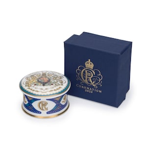Può includere: Una scatola portaoggetti in porcellana bianca con un design blu e oro che presenta lo stemma reale e la scritta "CORONATION 2023". La scatola è in una scatola di presentazione blu.